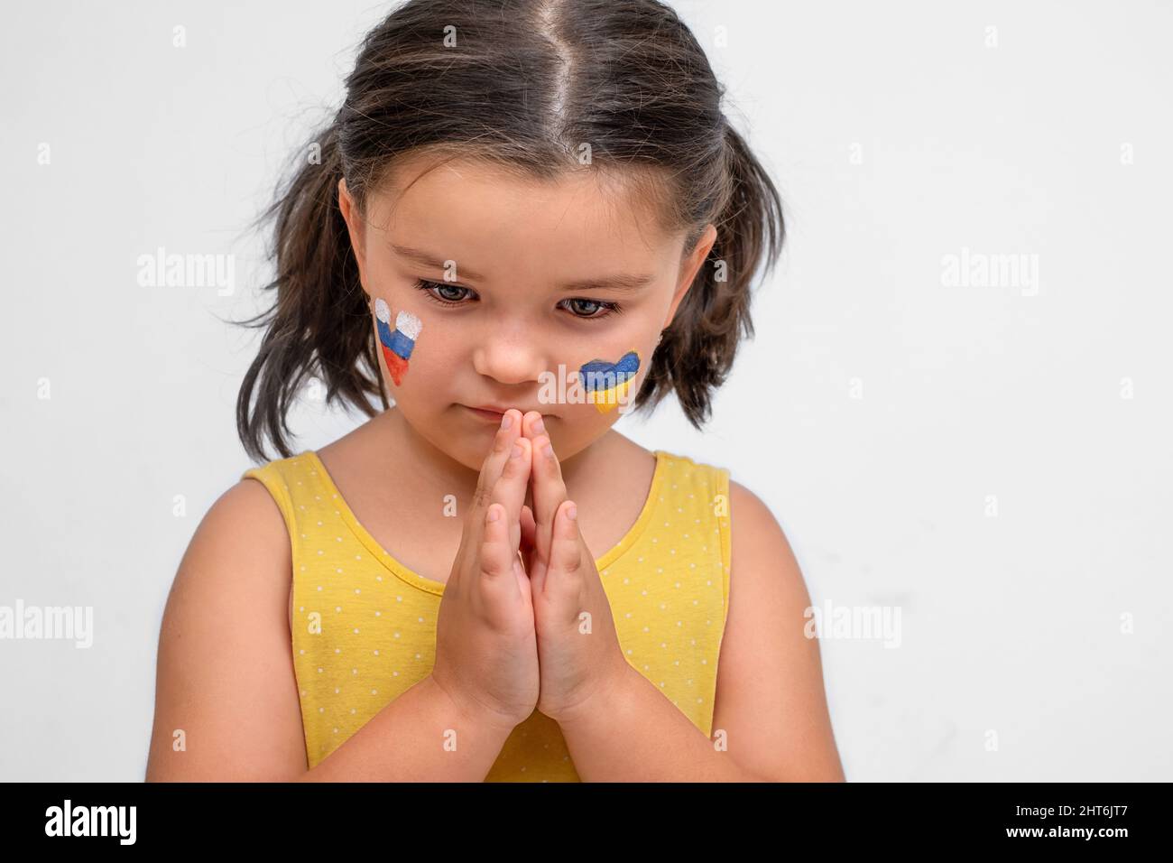 Un enfant triste aux coeurs ukrainiens et russes prie sur fond gris Banque D'Images