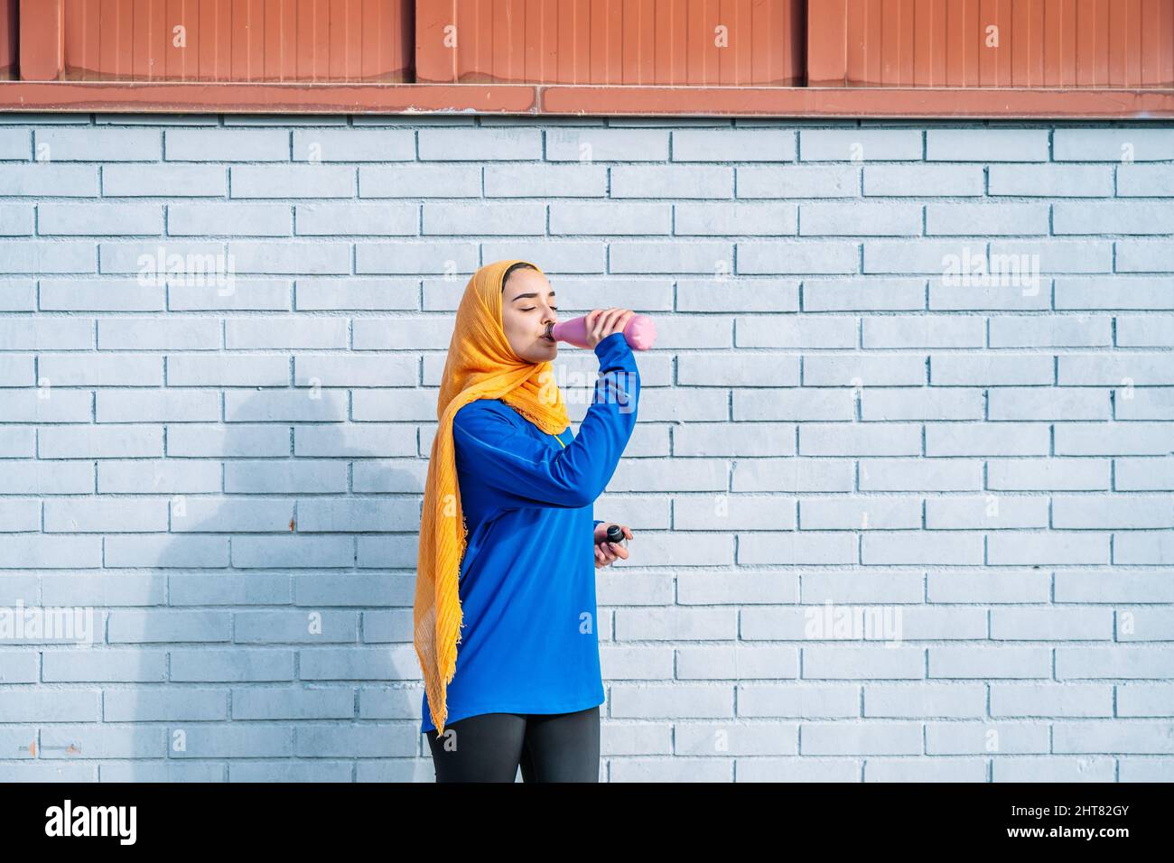 Femme arabe buvant de l'eau près du mur de briques pendant l'entraînement Banque D'Images