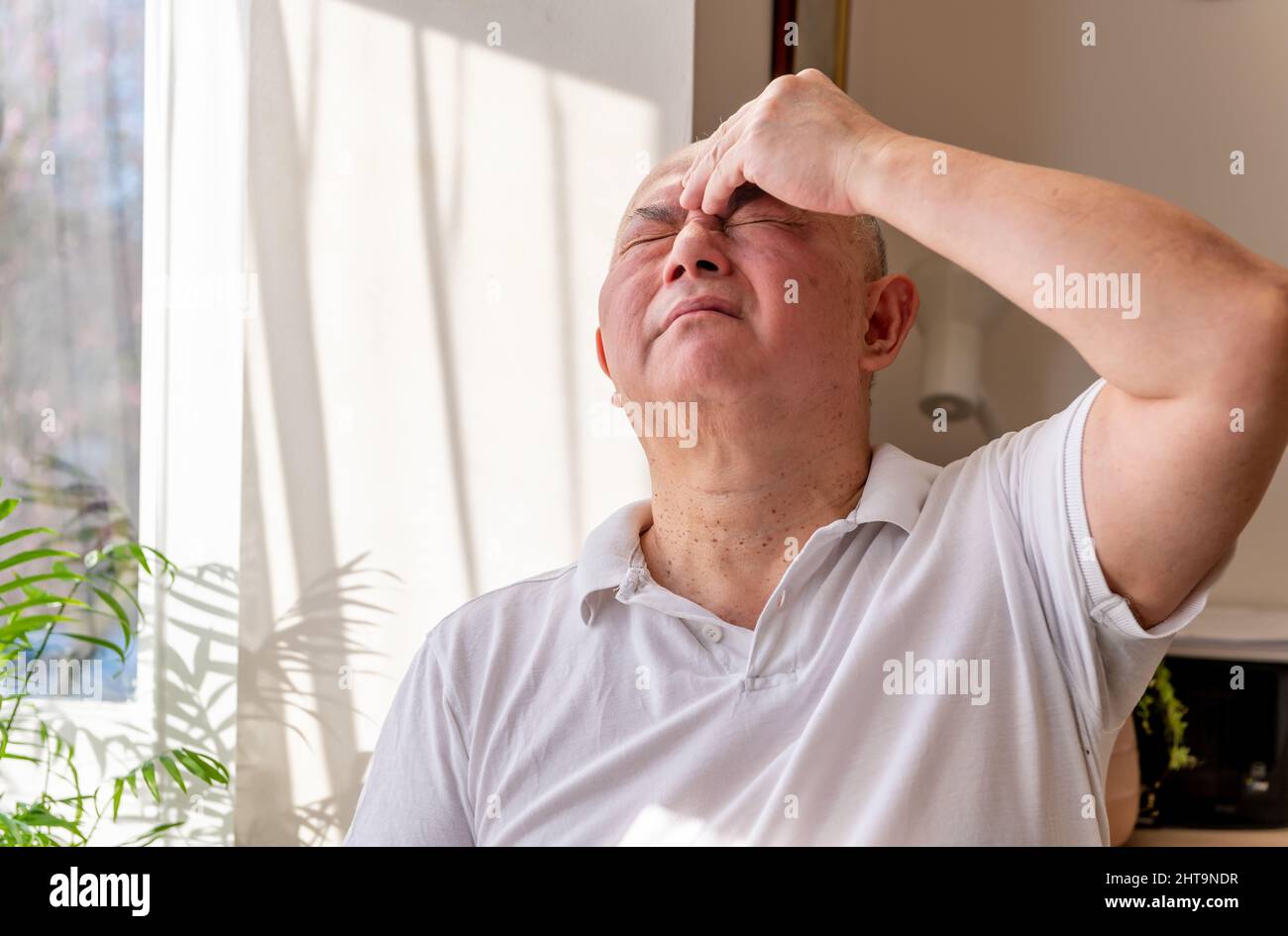 Un homme âgé mûr à la maison pinçant et frottant sa tête se sentant mal et ou dans la douleur. Concept de malaise. Banque D'Images