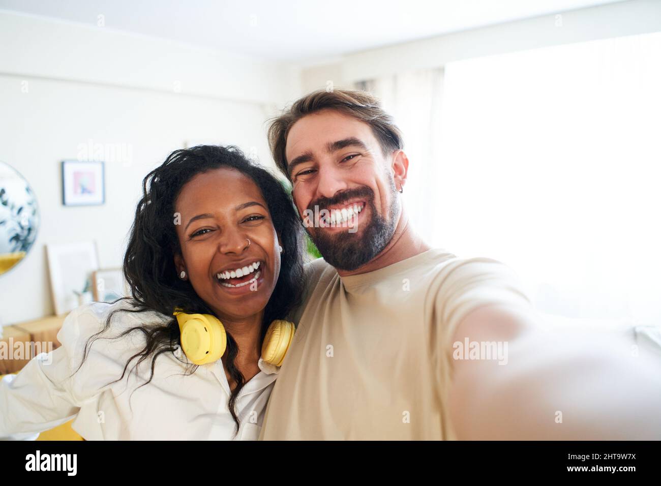 Joyeux selfie à la maison mixte couple de course souriant et regardant l'appareil photo. Un homme heureux et une belle femme qui prend des photos de soi et s'amuser Banque D'Images