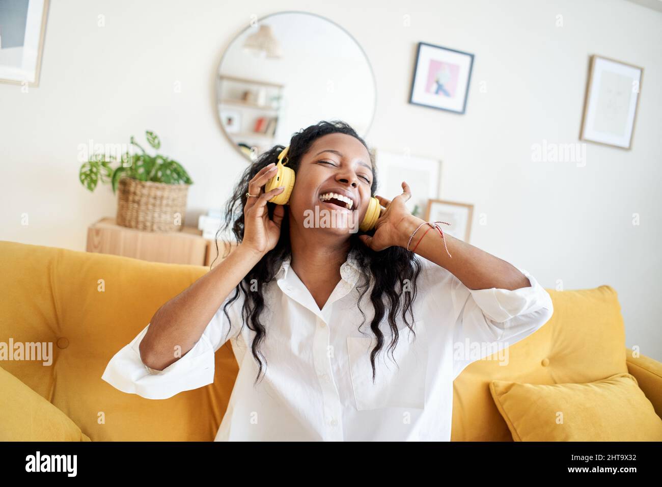 Jeune femme joyeuse écoutant de la musique avec un casque et dansant sur un canapé confortable à la maison dans la journée. Banque D'Images