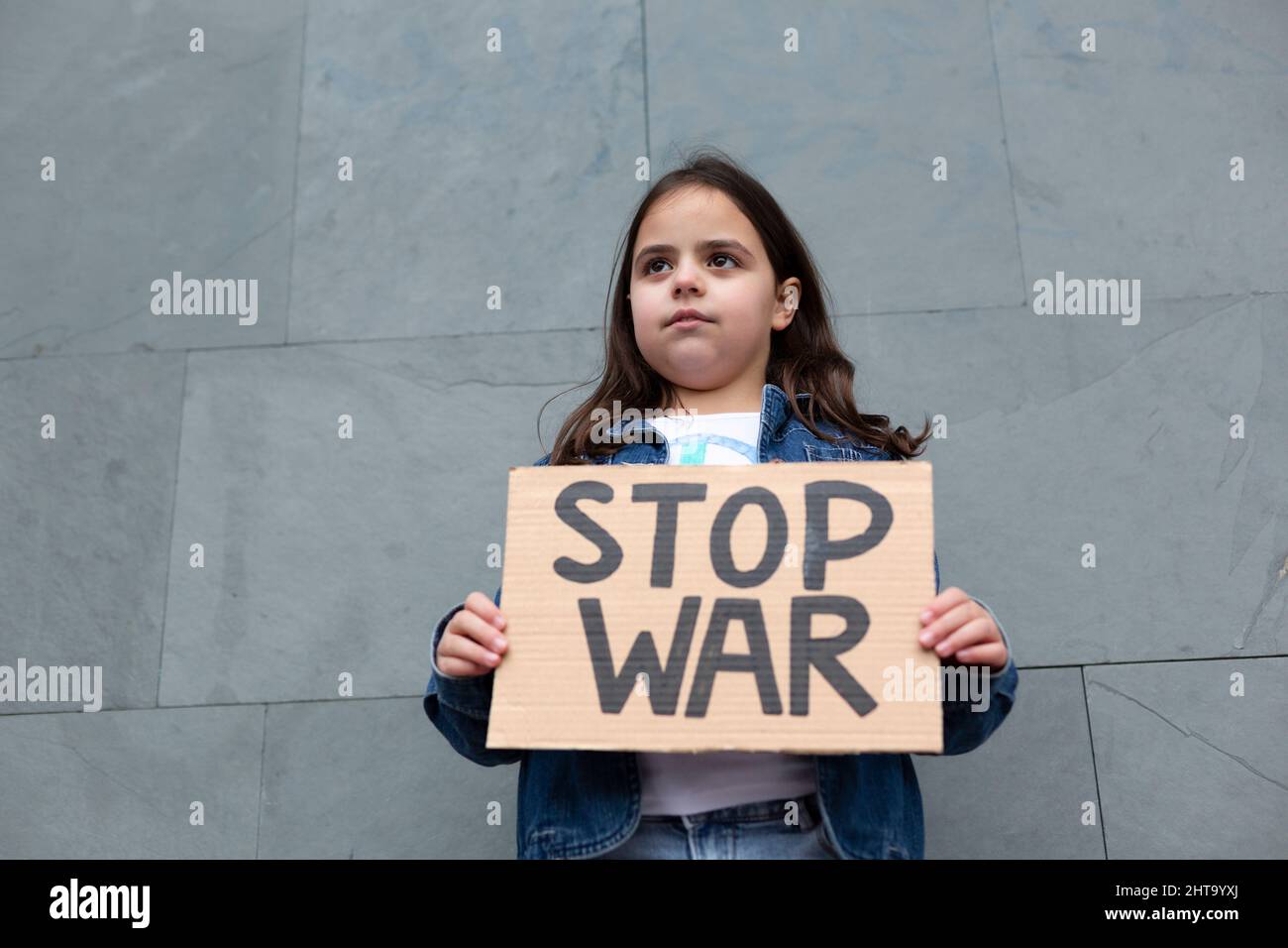 Petite fille caucasienne manifestant contre la guerre. Elle est dans la rue avec un panneau fait à la main. Banque D'Images