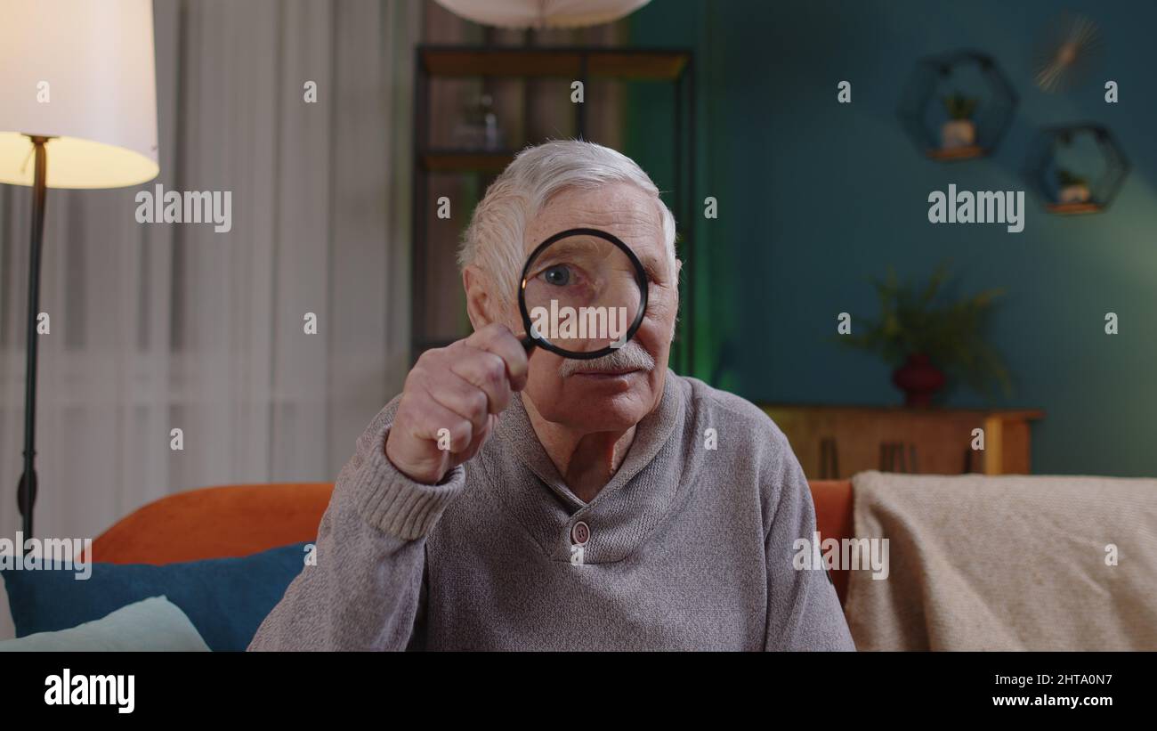 Grand-père senior homme regardant à travers la loupe, la lecture, la recherche, l'examen à la maison Banque D'Images