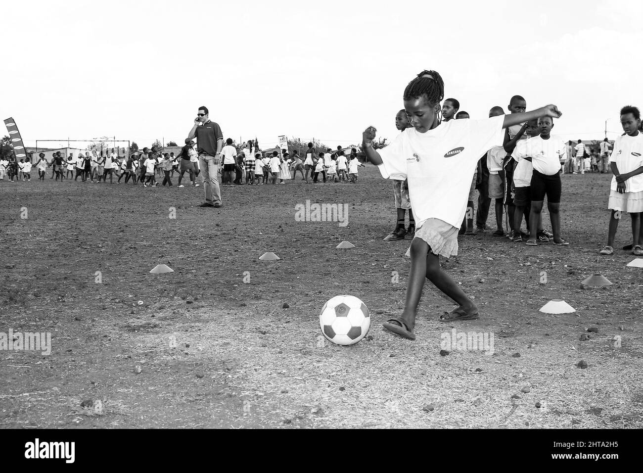 Prise de vue en niveaux de gris de jeunes enfants africains effectuant des activités de football sur un terrain de jeu scolaire Banque D'Images