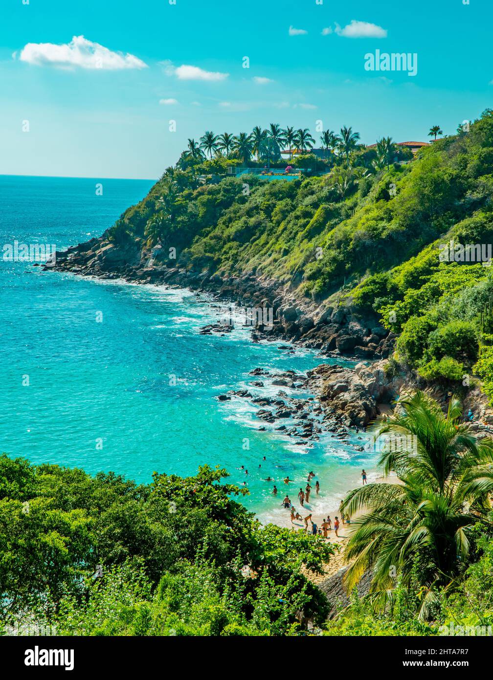 Un plan vertical d'une mer ou d'un océan avec des gens sur la plage et des arbres sur les rochers autour Banque D'Images