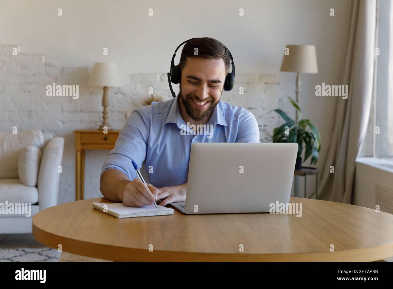 Un homme s'assoit au bureau avec un ordinateur portable pour prendre des notes dans un livre publicitaire Banque D'Images