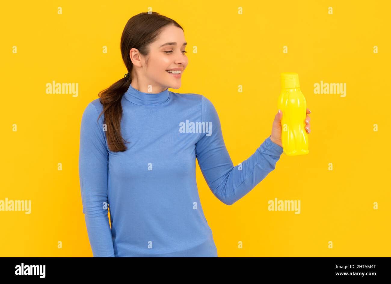 une femme souriante tient de l'eau minérale. elle a soif. jeune femme avec une bouteille de sport en plastique. Banque D'Images