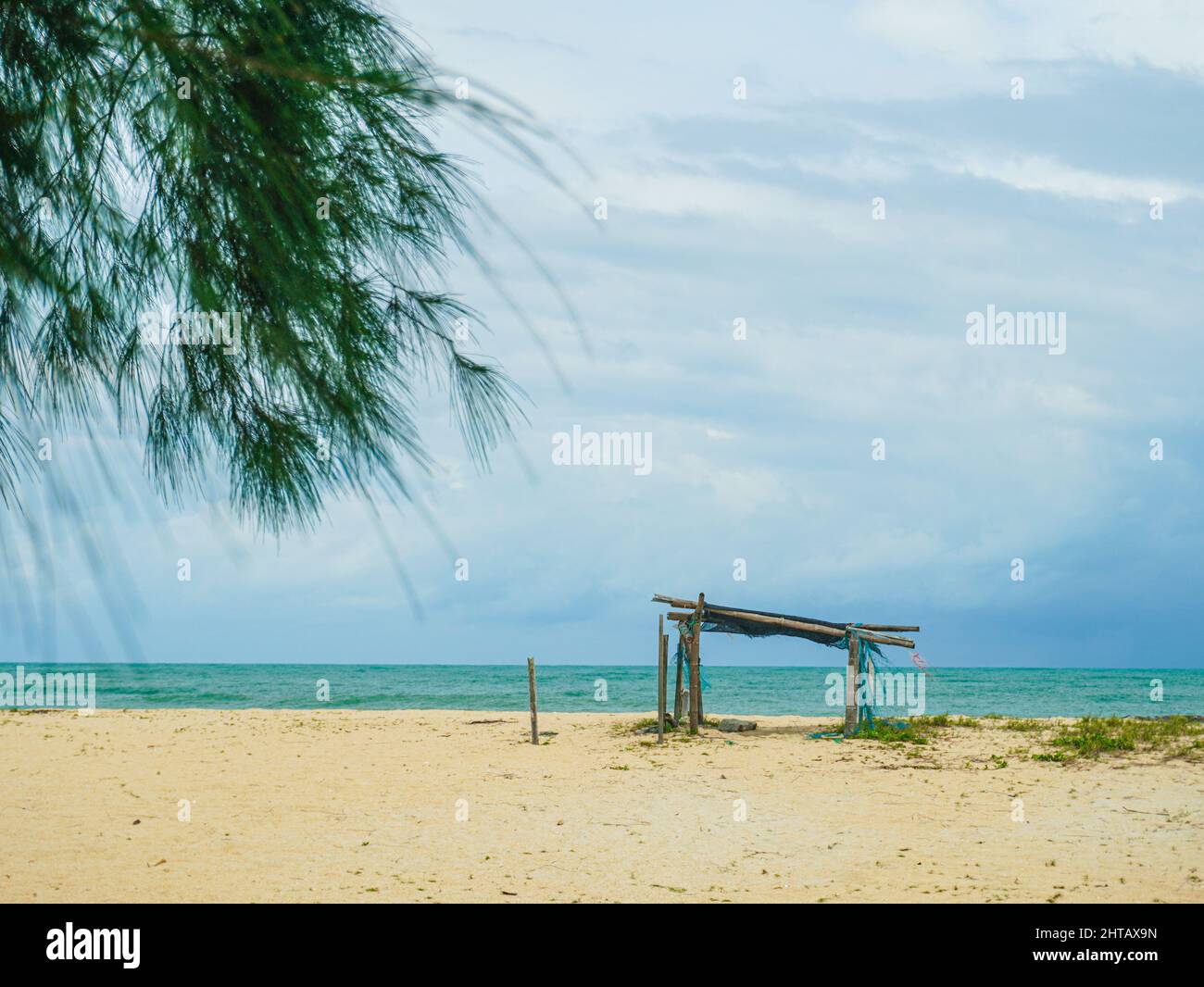 Une vue panoramique sur une plage de sable avec une structure en bois et une mer calme avec un ciel nuageux et clair en arrière-plan Banque D'Images