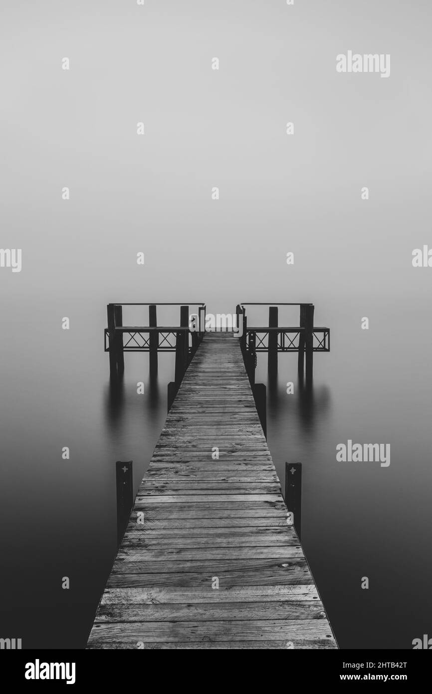 Échelle de gris d'un quai sur un lac par une journée brumeuse Banque D'Images
