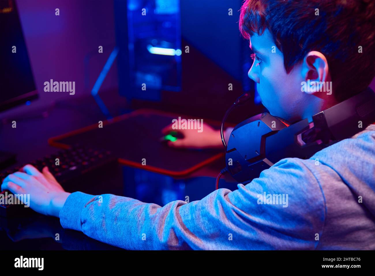 Un adolescent joue à un jeu vidéo informatique dans une pièce sombre,  utilise un clavier mécanique rvb couleur néon, un espace de travail pour  les jeux de cybersport, la dépendance des enfants