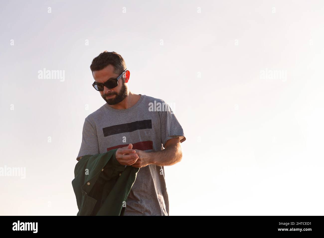 beau homme en lunettes de soleil en train de retirer sa veste avec le ciel en arrière-plan, concept de loisirs et de détente, copier l'espace pour le texte Banque D'Images