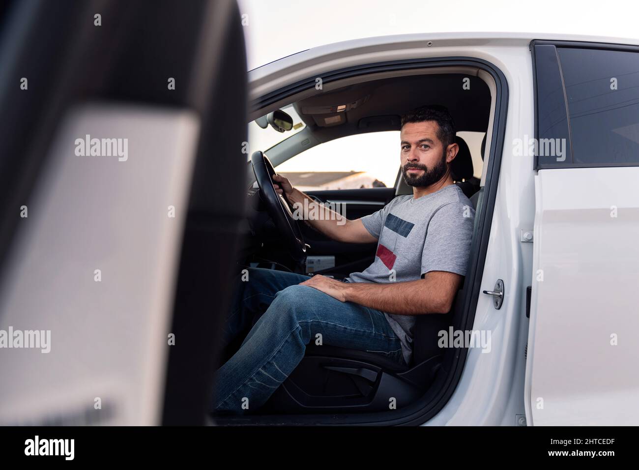 beau jeune homme barbu regardant sérieusement la caméra assis derrière le volant de sa voiture, de loisirs et de conduite concept Banque D'Images