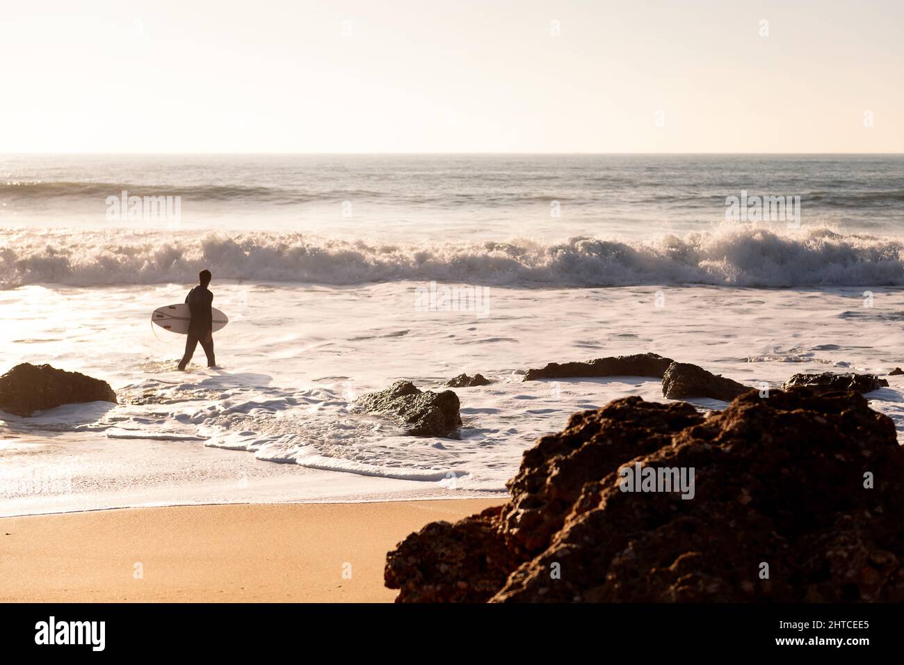 surfeur méconnaissable marchant le long du rivage de la plage avec sa planche sous son bras au coucher du soleil, concept de loisirs et de détente, copier l'espace pour le texte Banque D'Images