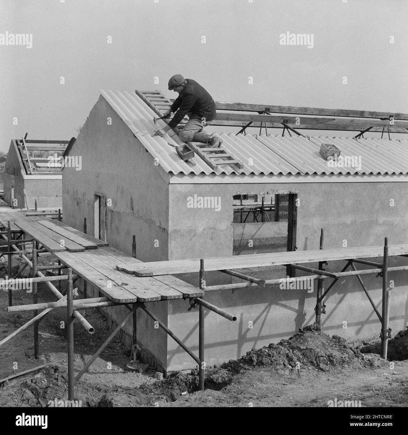 RAF Gaydon, Gaydon, Stratford-on-Avon, Warwickshire, 11/03/1953. Un homme qui pose des panneaux de toiture ondulés sur le toit d'un bâtiment nouvellement construit à Gaydon Airfield. Les travaux de construction d'une nouvelle piste à l'aérodrome de Gaydon ont commencé au début de 1952. Ce contrat a été suivi d'un deuxième contrat pour la construction de plus de 100 bâtiments du Ministère de l'air et de l'Easiform, et de 23 refuges de Nissen. Banque D'Images