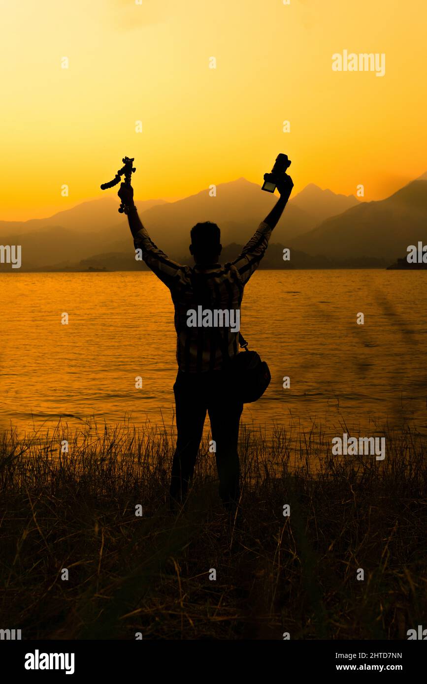 Photographe de la nature tenir le trépied avec l'appareil photo, voyageur profitant de la vue magnifique coucher du soleil, cliquez sur le barrage de Banasura Wayanad Kerala, Journée mondiale de la photographie Banque D'Images