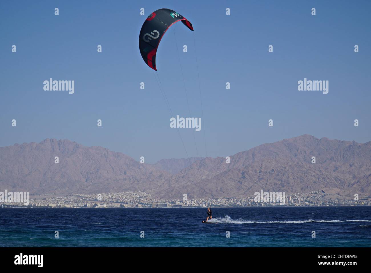 La planche à voile dans la mer d'Eilat, Israël avec la ville d'Aqaba en Jordanie en arrière-plan Banque D'Images