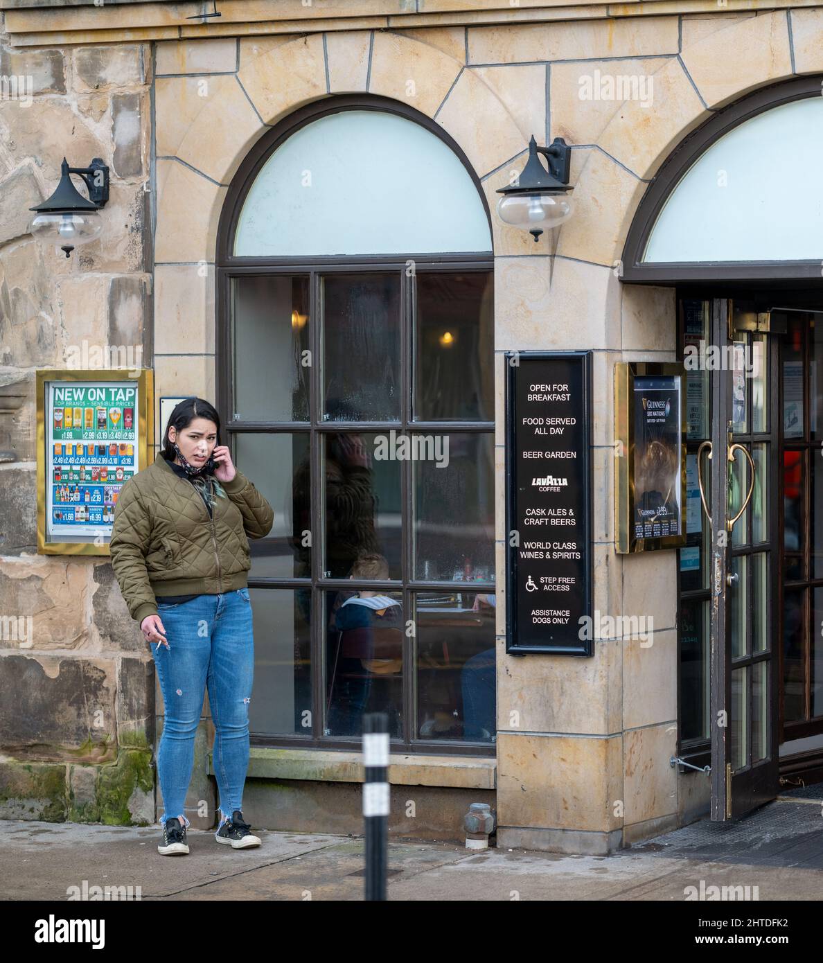 25 février 2022. High Street, Elgin, Moray, Écosse. C'est une femme qui est allée à l'extérieur du Pub pour avoir une fumée tout en bavardant sur son téléphone mobile Banque D'Images