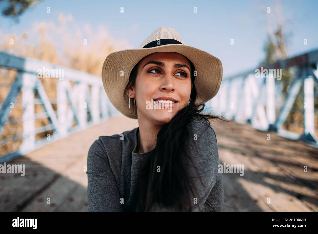 Une femme hispanique rêveuse dans un chapeau assis sur un quai au bord de la rivière Banque D'Images