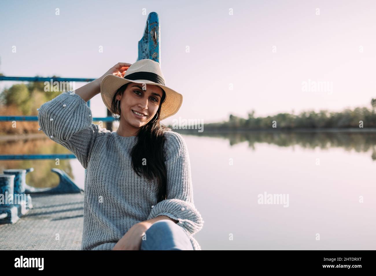 Portrait d'une femme hispanique souriant avec un chapeau sur le bord d'un quai à côté d'un lac Banque D'Images