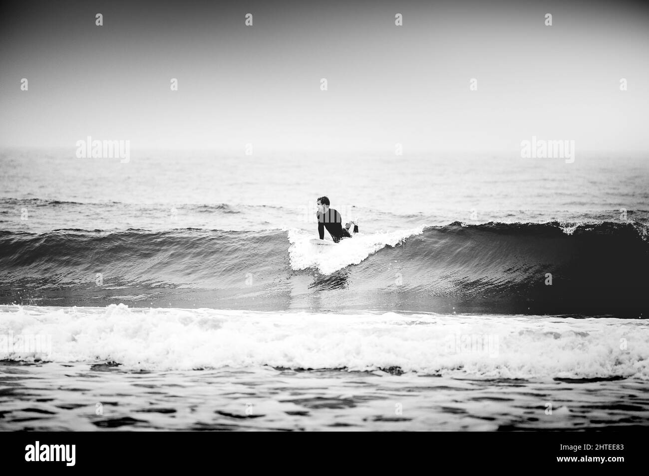 Photo en niveaux de gris du surfeur qui frappe les vagues à Newport Beach en Californie Banque D'Images