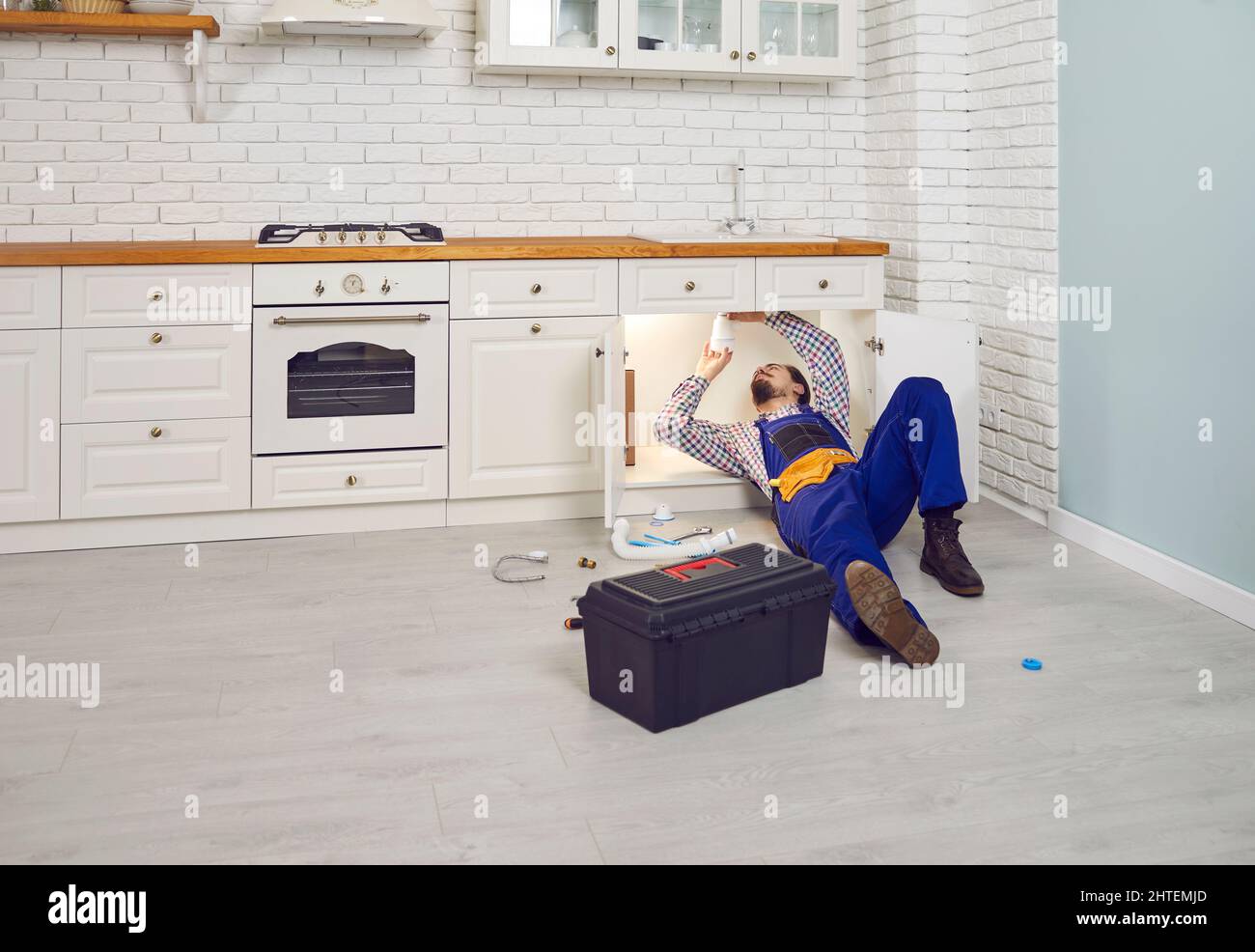 Plombier couché sur le sol sous l'évier de la cuisine et nettoyage de l'égout bouché Banque D'Images