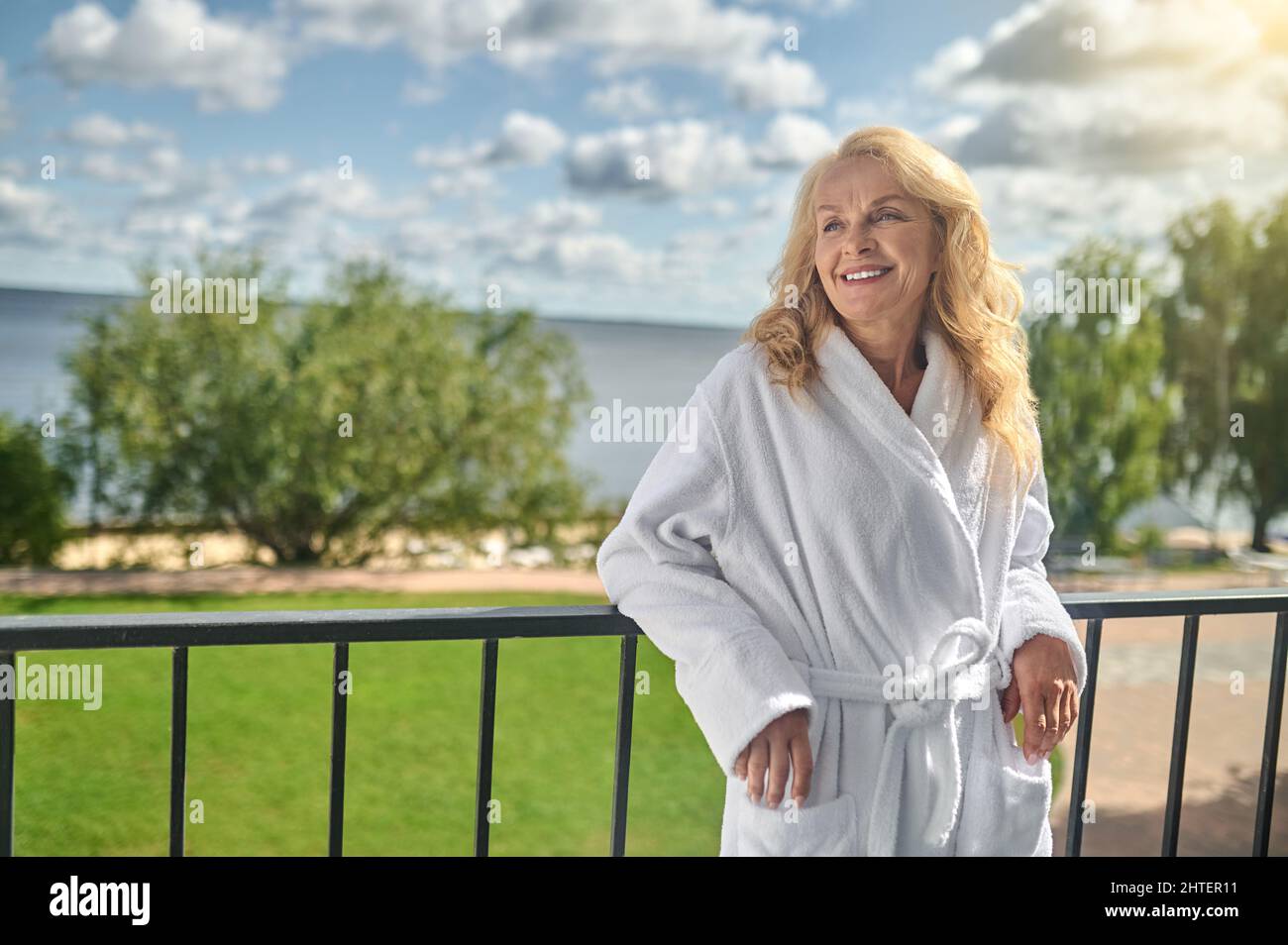 Une femme blonde dans un peignoir blanc debout sur le balcon Banque D'Images