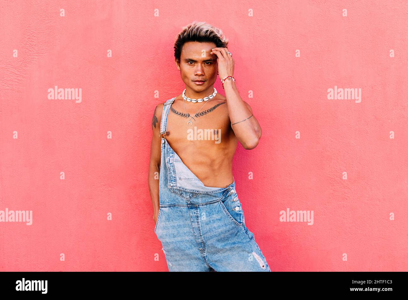Un adorable gars portant une combinaison en denim se posant sur fond rose Banque D'Images