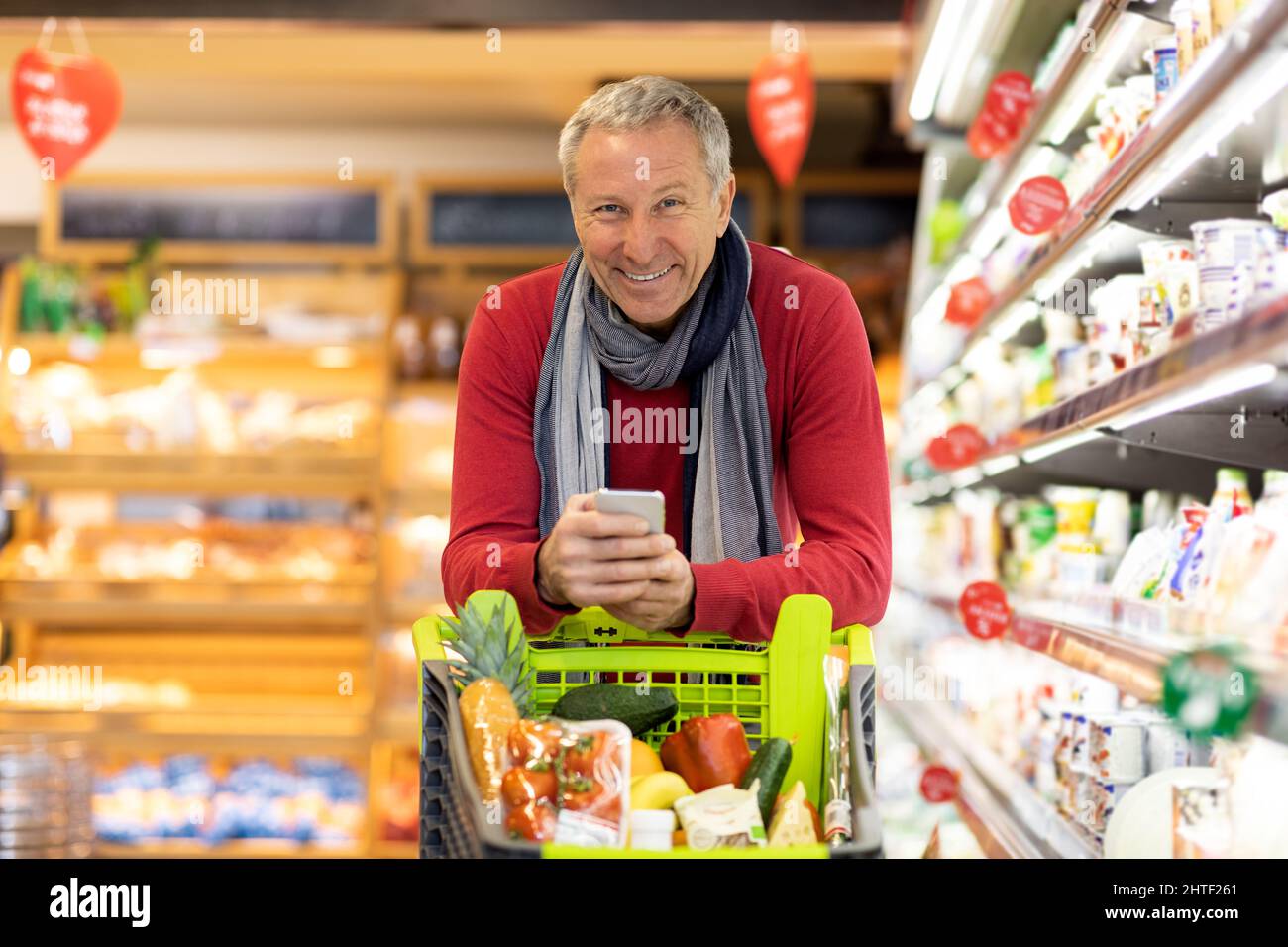 Joyeux homme âgé magasiner au supermarché, tenant un smartphone Banque D'Images