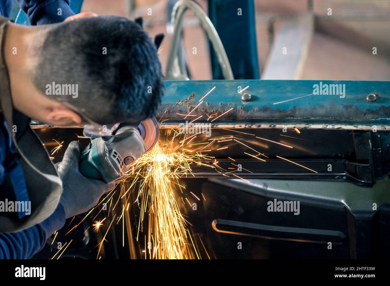 Jeune homme travailleur mécanique répare une vieille carrosserie de voiture d'époque Dans un garage désordonné - sécurité au travail avec vêtements de protection Banque D'Images