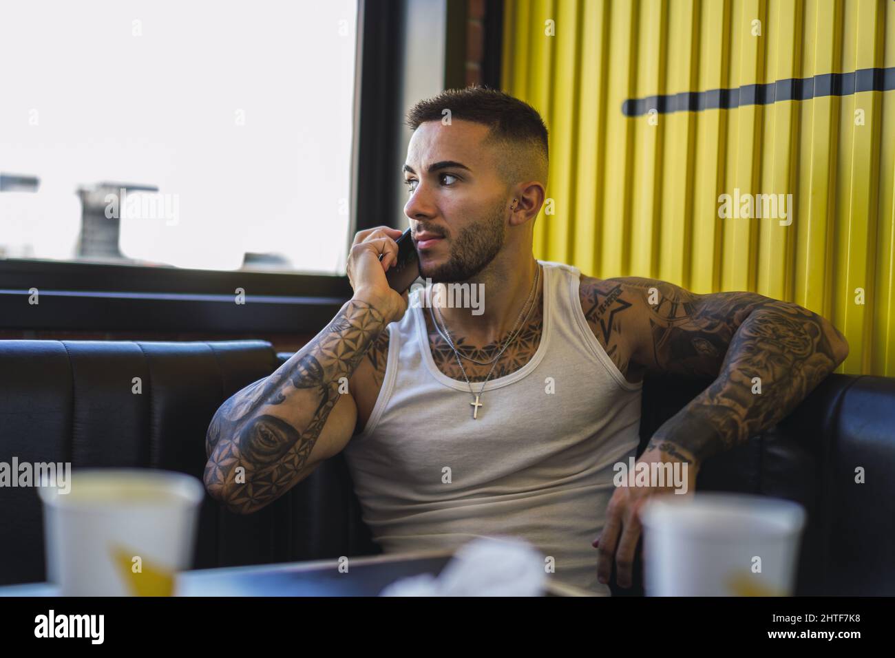 Jeune homme caucasien avec des tatouages frais assis dans le café parlant au téléphone Banque D'Images