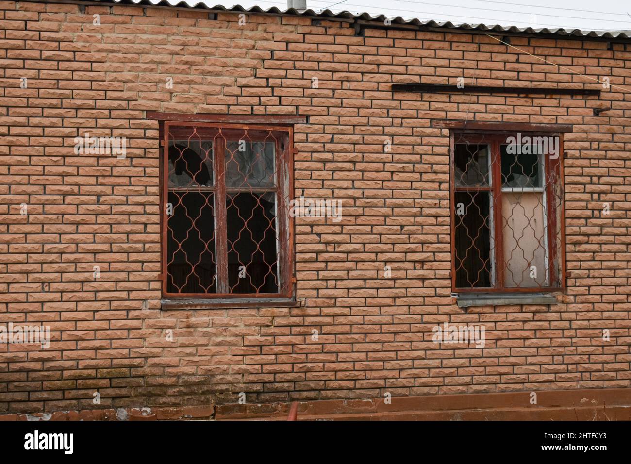 Deux fenêtres brisées avec un vieux cadre en bois sur le mur de briques de la maison après l'explosion. Banque D'Images