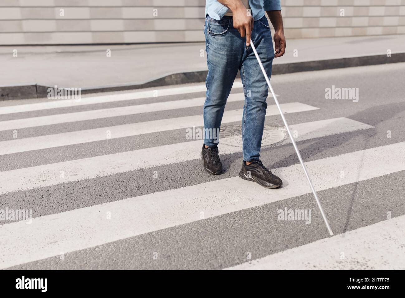 Jeune homme noir méconnaissable avec un handicap visuel marchant dans la rue de la ville, en utilisant la canne à pied à l'extérieur, l'espace de copie Banque D'Images