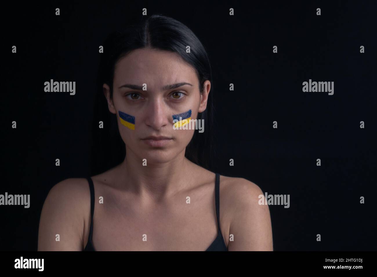 Portrait d'une femme ukrainienne sérieuse avec un drapeau ukrainien bleu et jaune sur sa joue. Le symbole de l'inviolabilité du peuple ukrainien. Ba foncé Banque D'Images