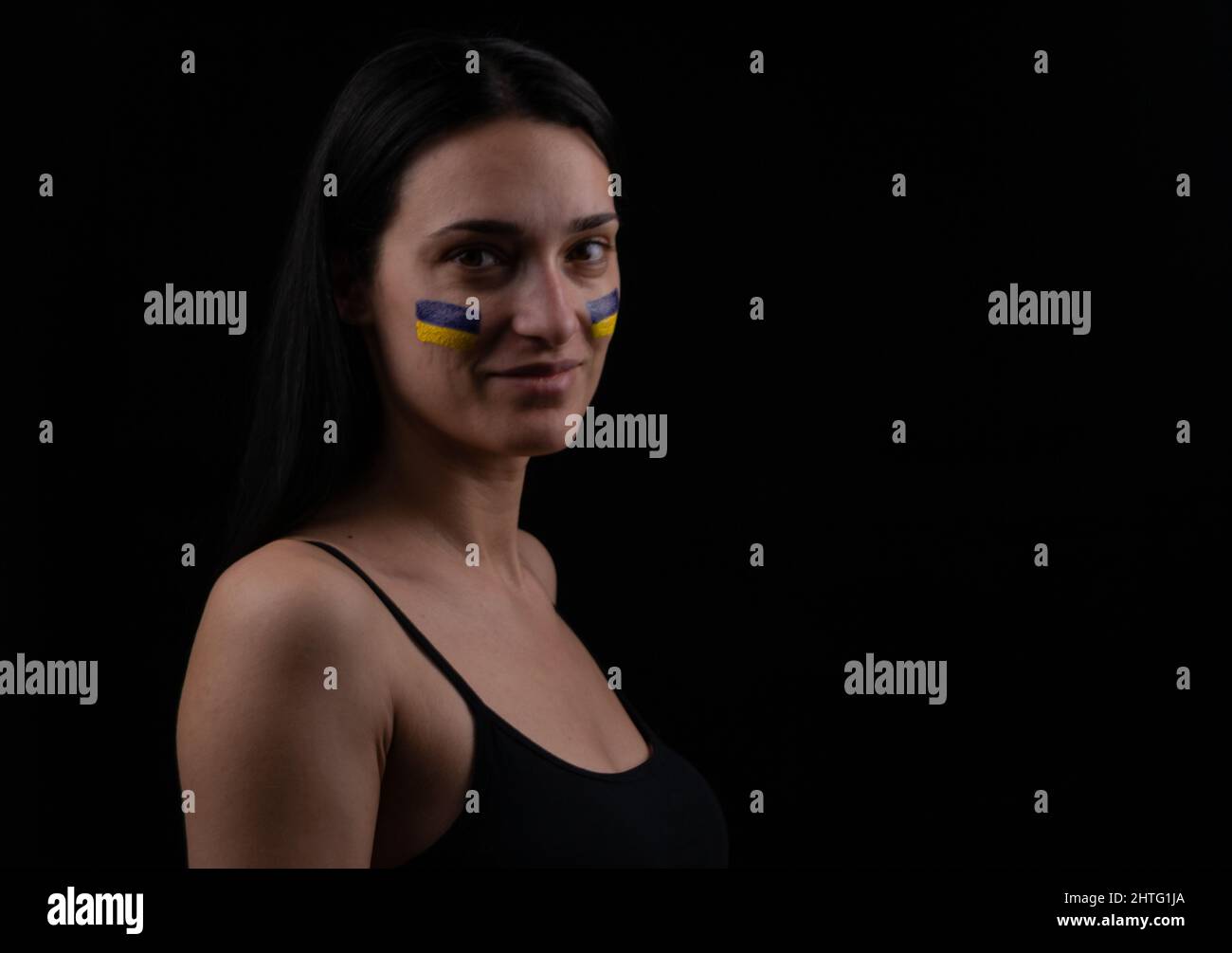 Portrait d'une femme souriante avec drapeau ukrainien bleu et jaune sur sa joue. Arrière-plan sombre. Espace pour le texte Banque D'Images