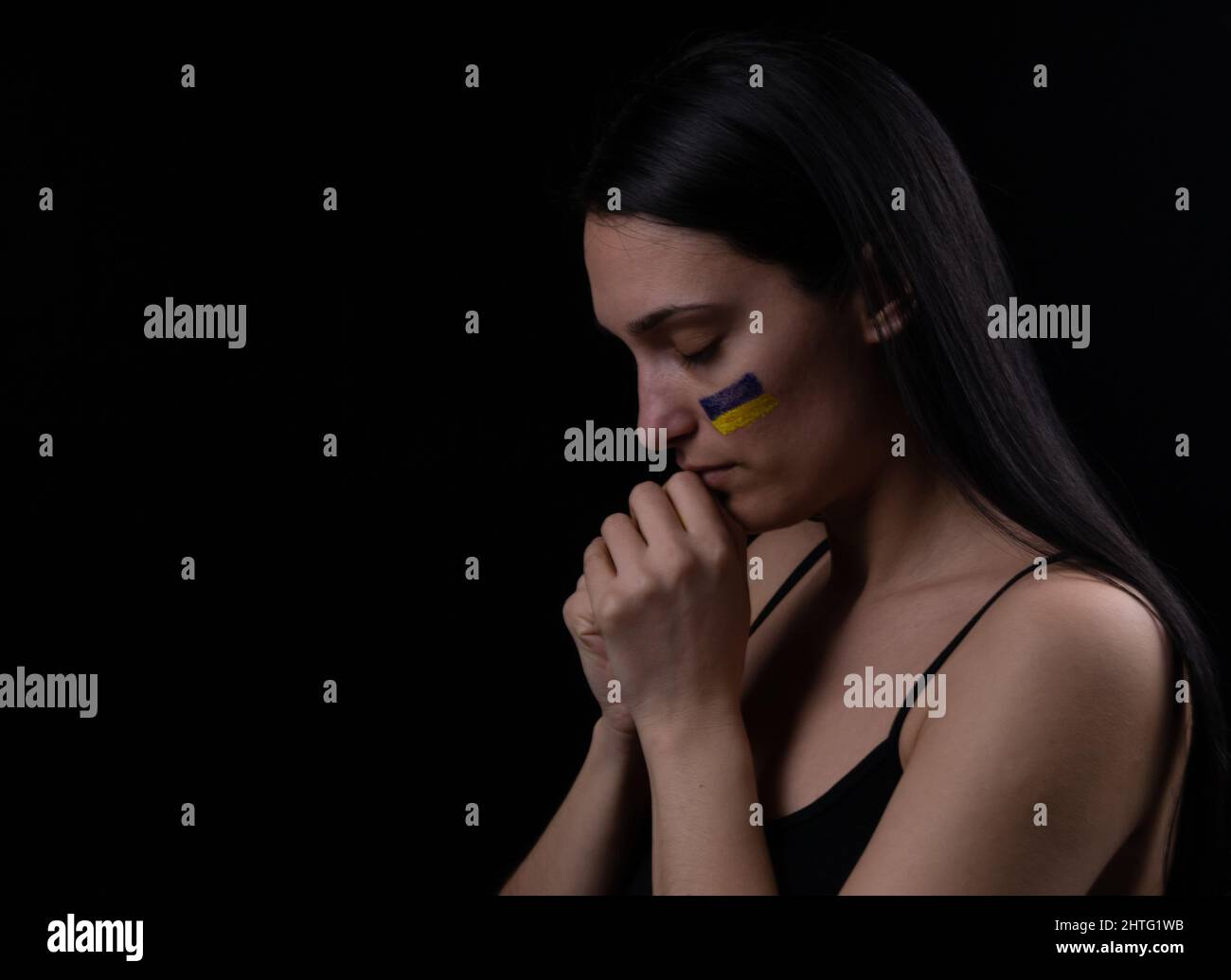 Portrait d'une femme ukrainienne avec un drapeau ukrainien bleu et jaune sur sa joue priant pour l'Ukraine. Le symbole de l'inviolabilité du peo ukrainien Banque D'Images