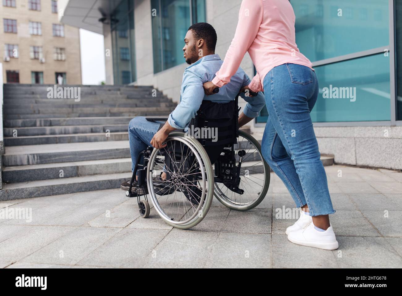 Jeune femme noire avec homme millénaire en fauteuil roulant n'ayant aucune possibilité d'entrer dans le bâtiment sans rampe, à l'extérieur Banque D'Images