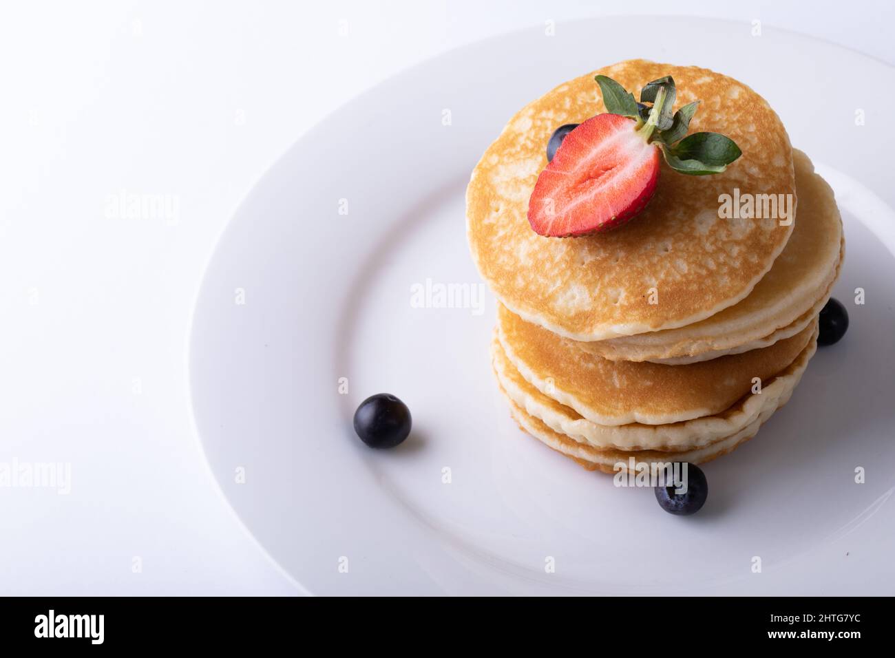 Vue en grand angle des crêpes empilées avec fruits rouges dans l'assiette sur fond blanc Banque D'Images