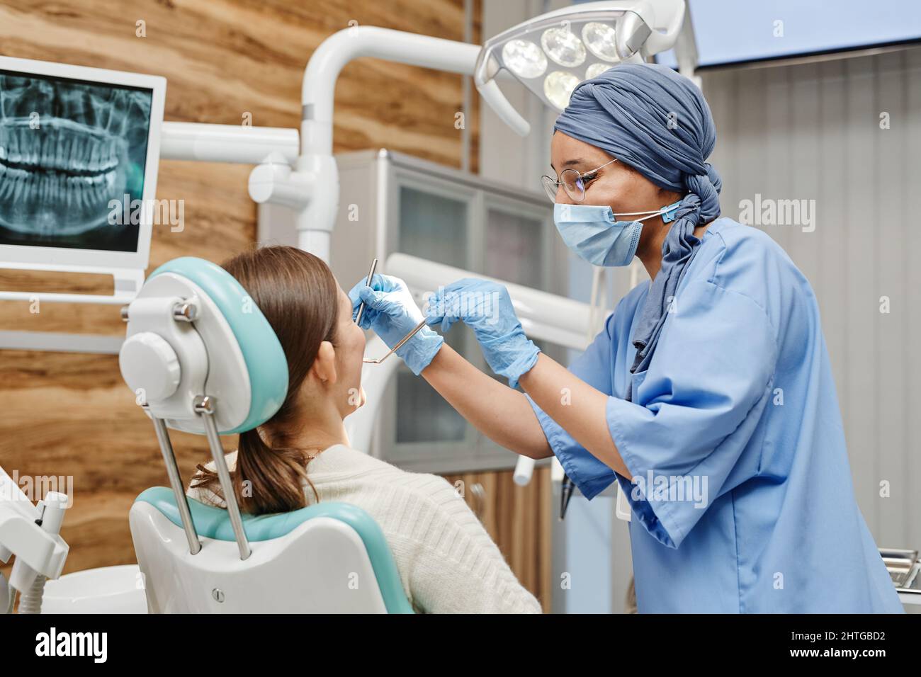 Portrait à la taille de la jeune femme dentiste examinant le patient assis dans une chaise à la clinique dentaire Banque D'Images