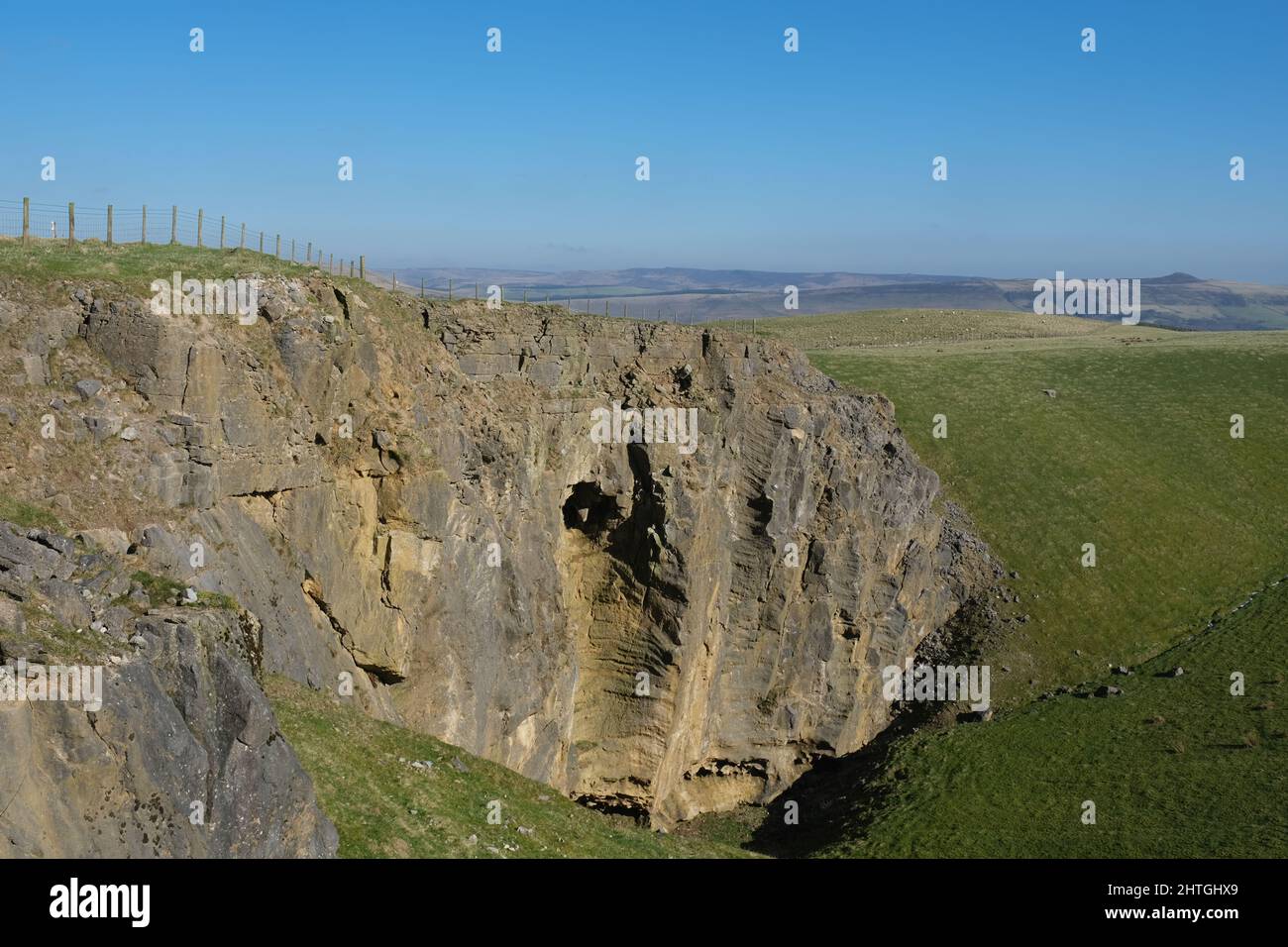 Carrière face près de Dirtlow Rake, près de Castleton, Derbyshire. Une immense face de roche rouge est clôturée d'en haut et montre les entrées de la grotte ci-dessous. Banque D'Images