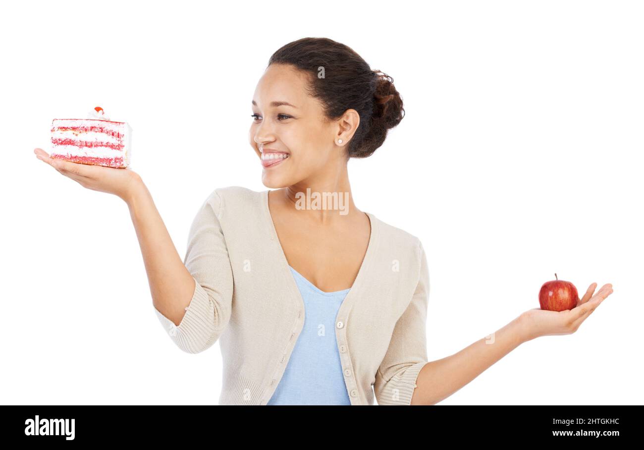 J'ai certainement ce gâteau. Jeune femme souriant tout en essayant de décider entre un morceau de gâteau et une pomme - isolée sur blanc. Banque D'Images