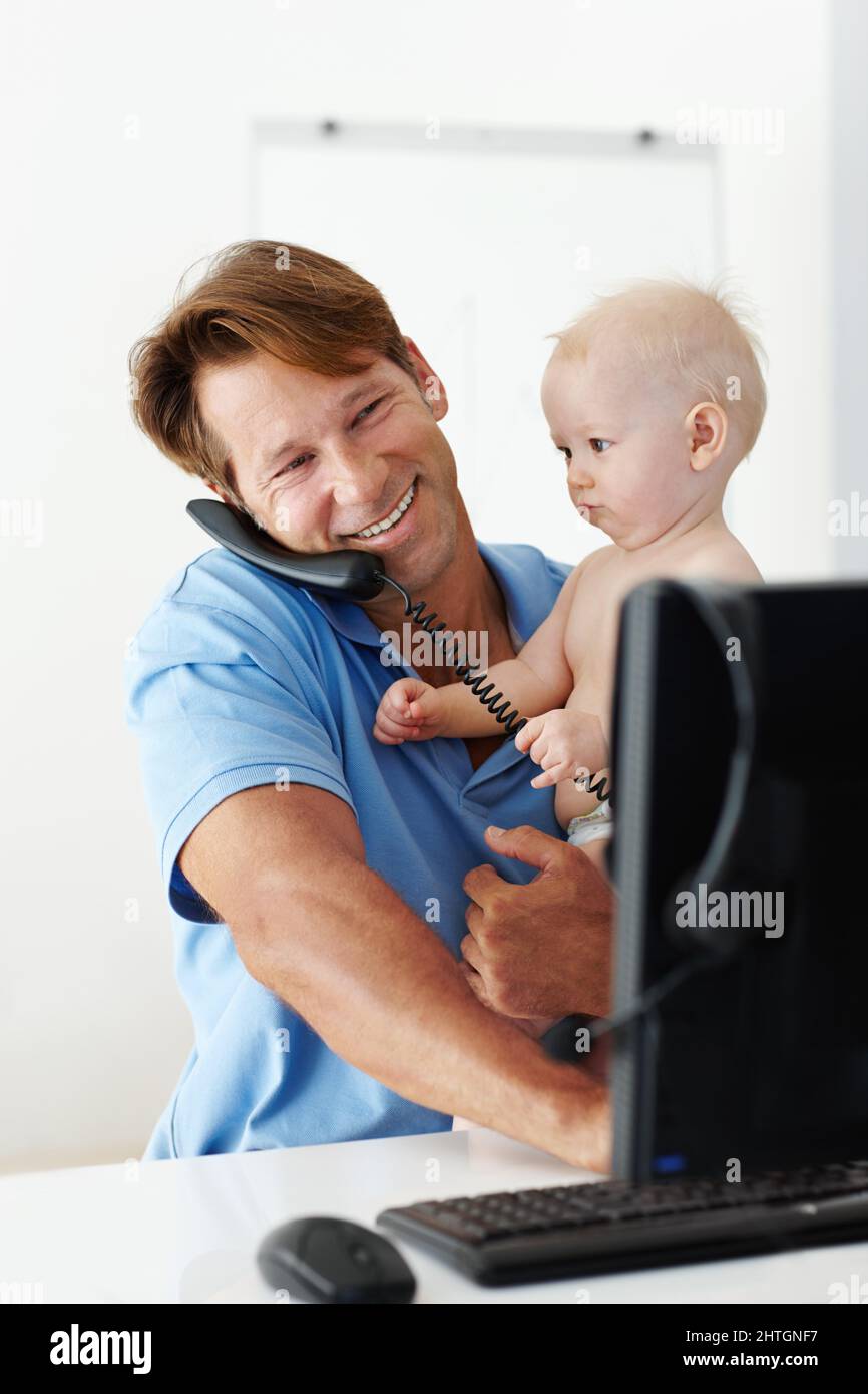 J'ai reçu un message important pour vous Papa. Photo d'un père à son bureau tenant un petit enfant tout en parlant au téléphone. Banque D'Images