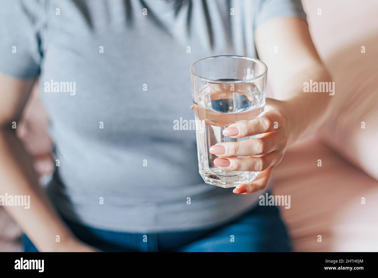 Une femme s'assoit dans son lit et tient un verre d'eau propre dans ses mains. Journée mondiale de l'eau. Concept de soins de santé. Boire de l'eau le matin pour stimuler le métabolisme. Banque D'Images