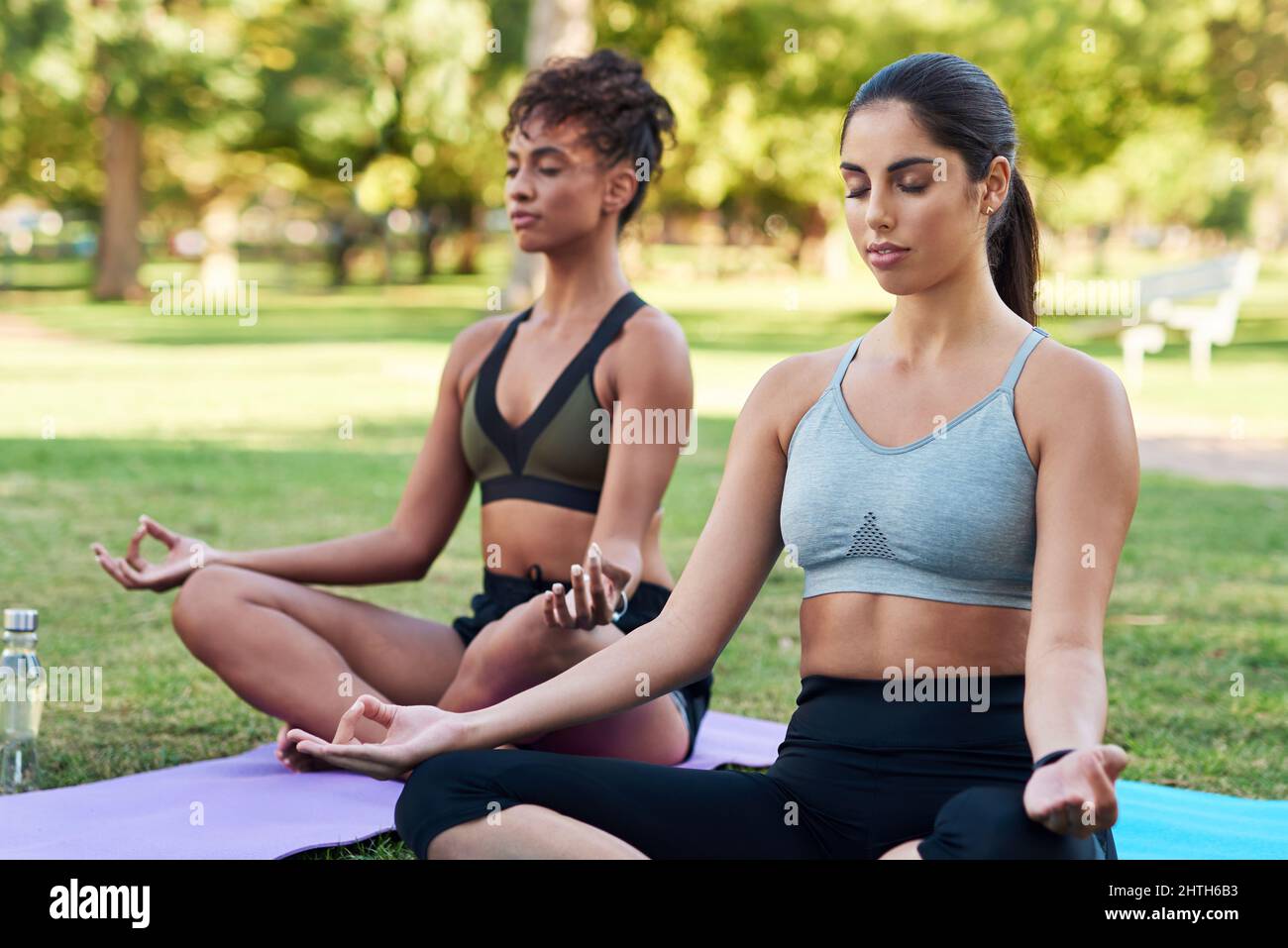 Se concentrer sur la pleine conscience et le souffle. Plan court de deux jeunes femmes attrayantes assises les unes à côté des autres et méditant dans le parc. Banque D'Images