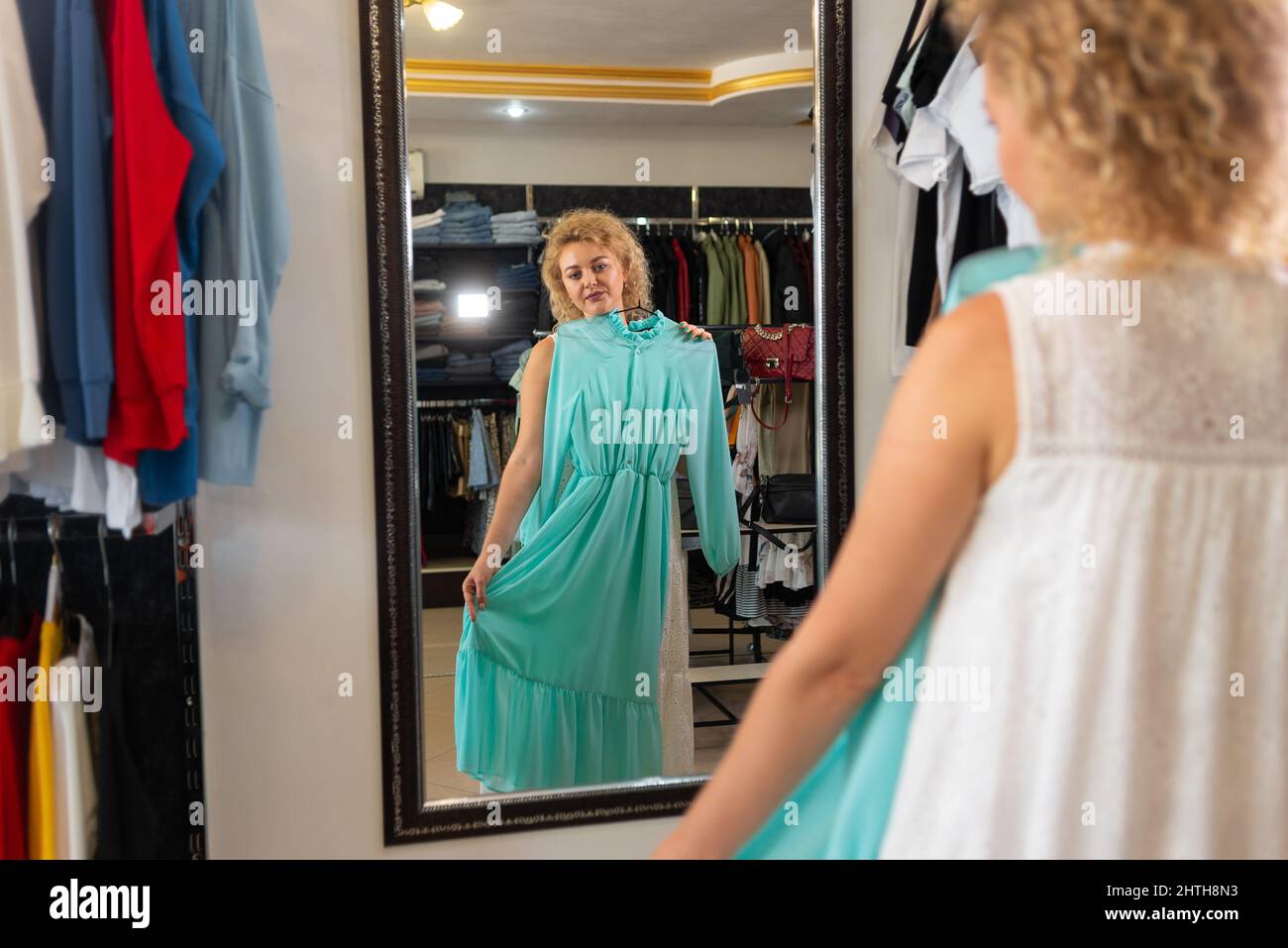 Une fille blonde essaie une robe devant un miroir dans un magasin de  vêtements, une cabine d'essayage dans une boutique de vêtements pour  femmes, en choisissant et en achetant un été d