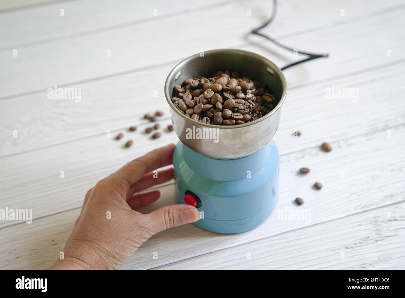 Grains de café à l'intérieur d'un moulin électrique, avec la main de femme à côté. Copier l'espace. Banque D'Images