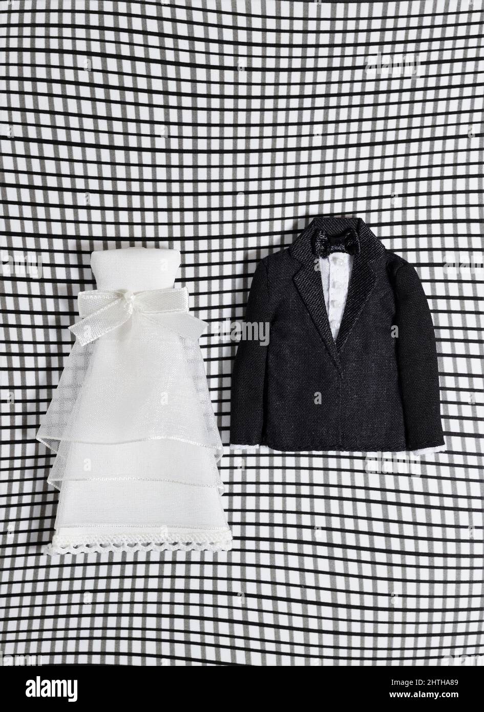 Une robe de mariage miniature et un smoking sur un fond de grille voilé. Banque D'Images