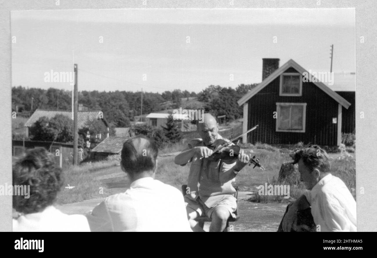 Photographie noir et blanc des années 60 d'un homme jouant un violon en plein air, sous la surveillance de deux hommes et d'une femme, la Suède. Concept de loisirs, de détente, d'antan Banque D'Images