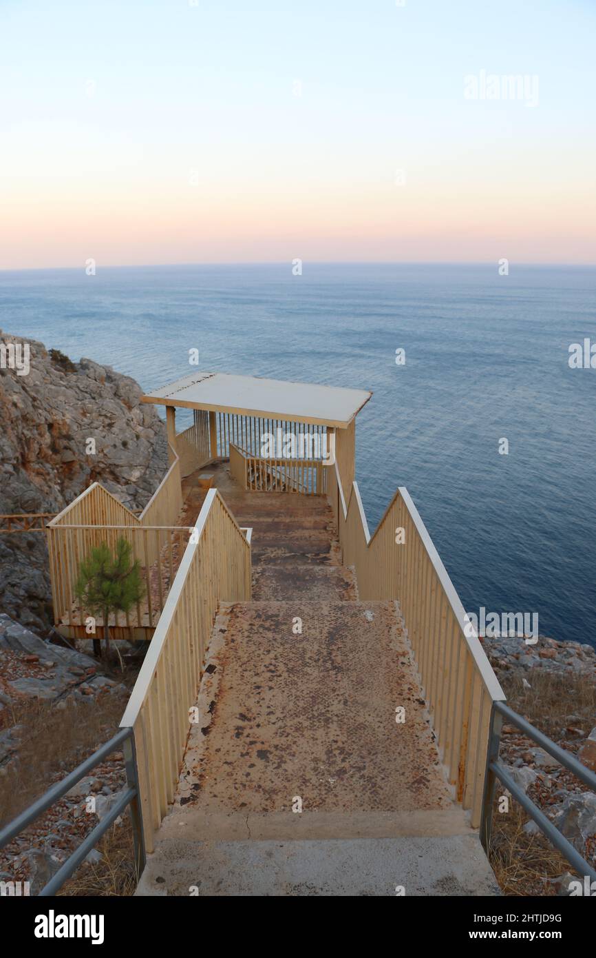 Les escaliers rouillés et jaunes vont au paradis avec une belle mer et des rochers. Une vue paisible et relaxante au coucher du soleil. Banque D'Images