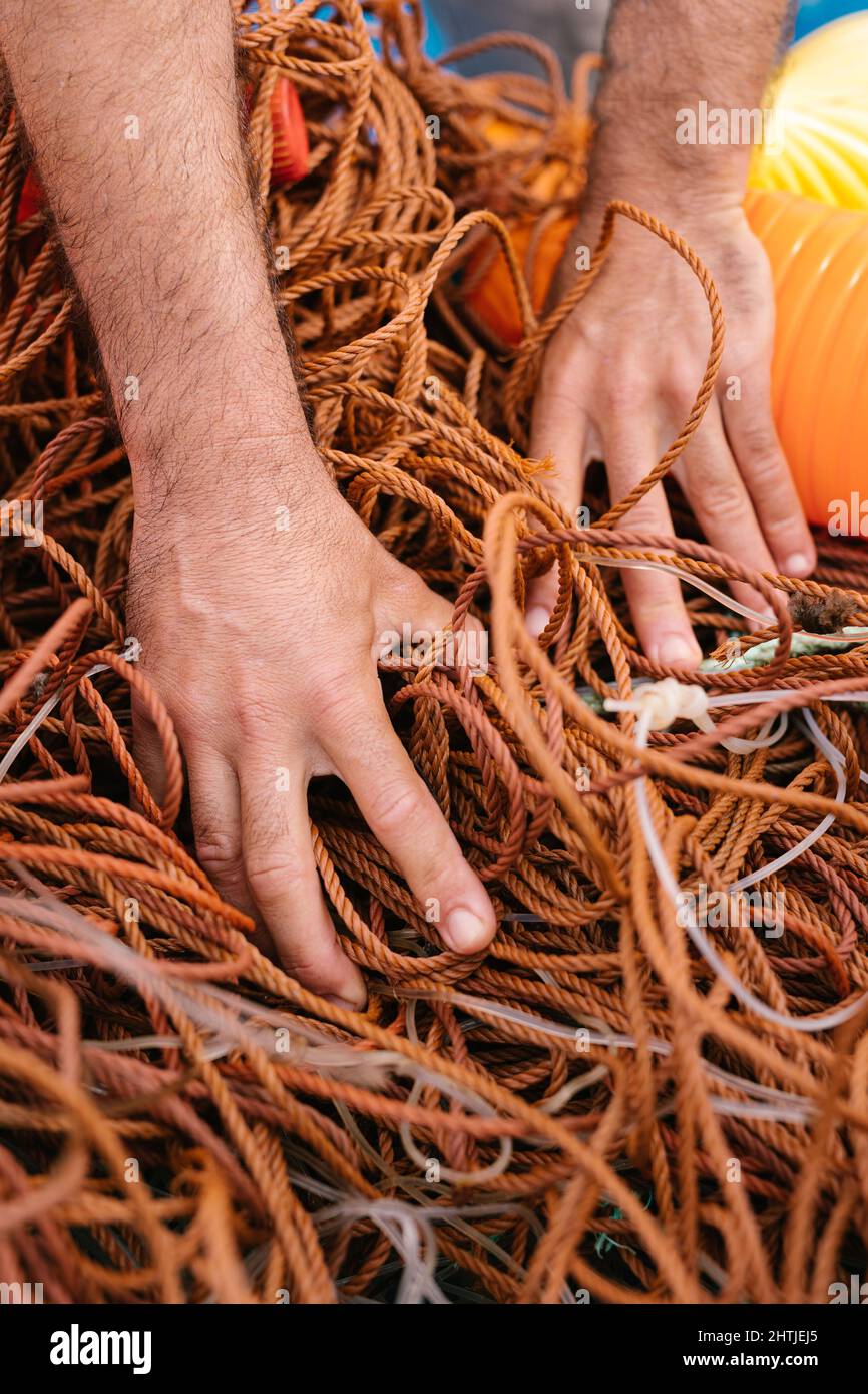 Grand angle de récolte pêcheur anonyme prenant pile de matériel de pêche emmêlé sur le bateau Banque D'Images
