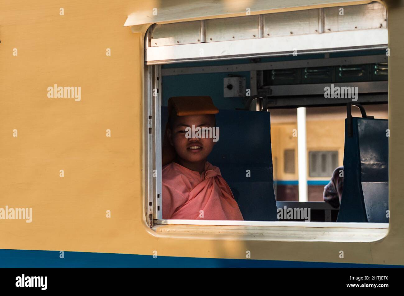 Mandalay, MYANMAR - 12 AVRIL 2017: Curieux bouddhibouin asiatique regardant la caméra à travers la fenêtre du train à la gare de Mandalay le jour ensoleillé Banque D'Images